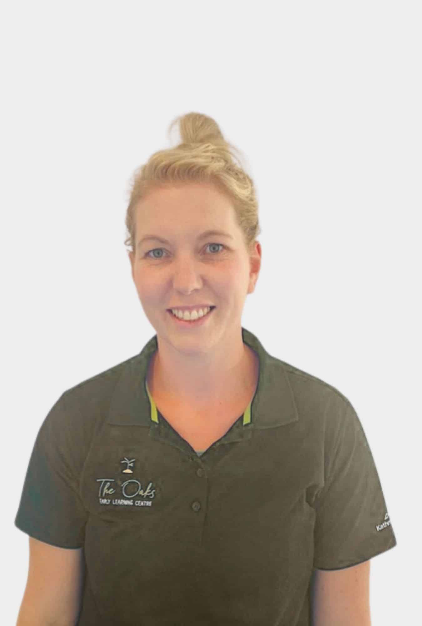 A woman with blonde hair in a bun, wearing a dark polo shirt with "The Oaks Early Learning Centre" logo, stands against a plain white background.